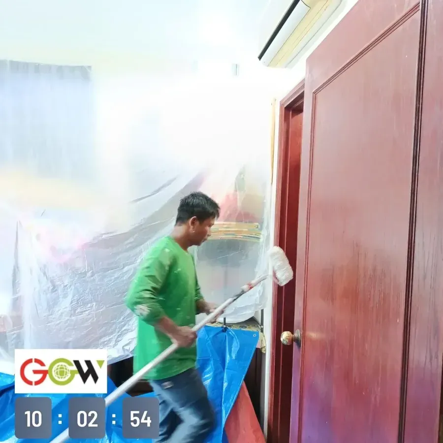 Crew member repainting an internal door with the room sheeted for protection